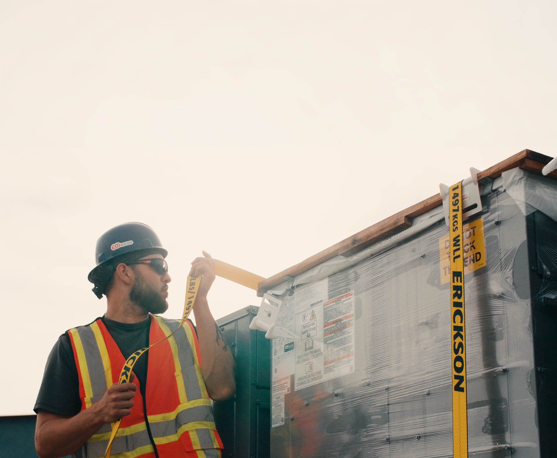 Technician unspooling a strap beside a wrapped rooftop unit